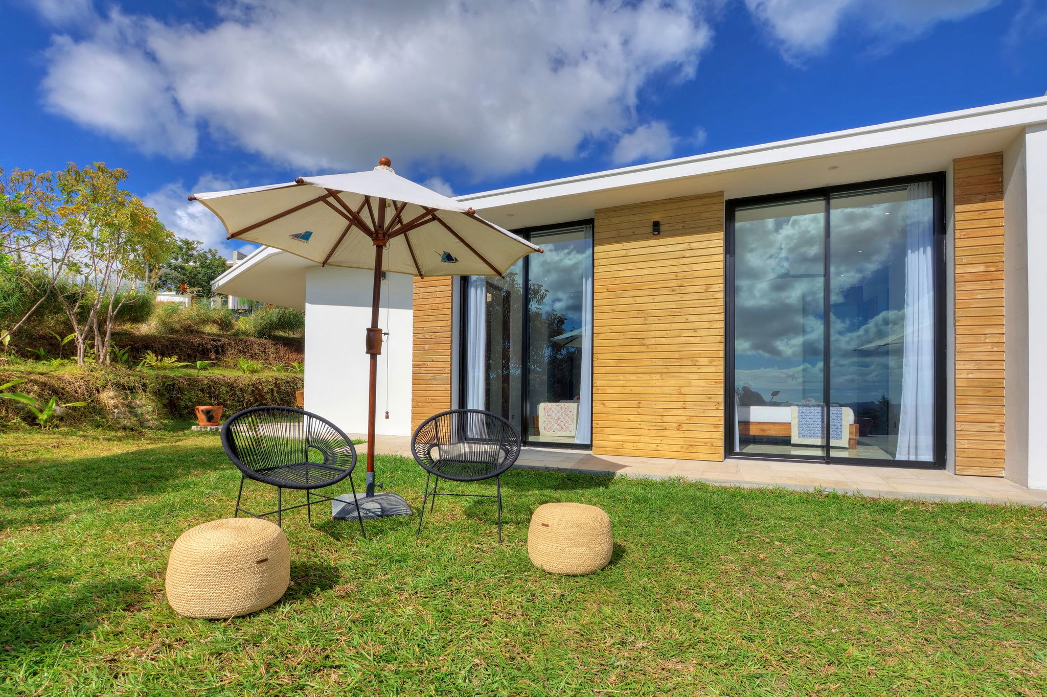 Una casa moderna con puerta de vidrio, un patio con dos sillas y una mesa, y una sombrilla grande.