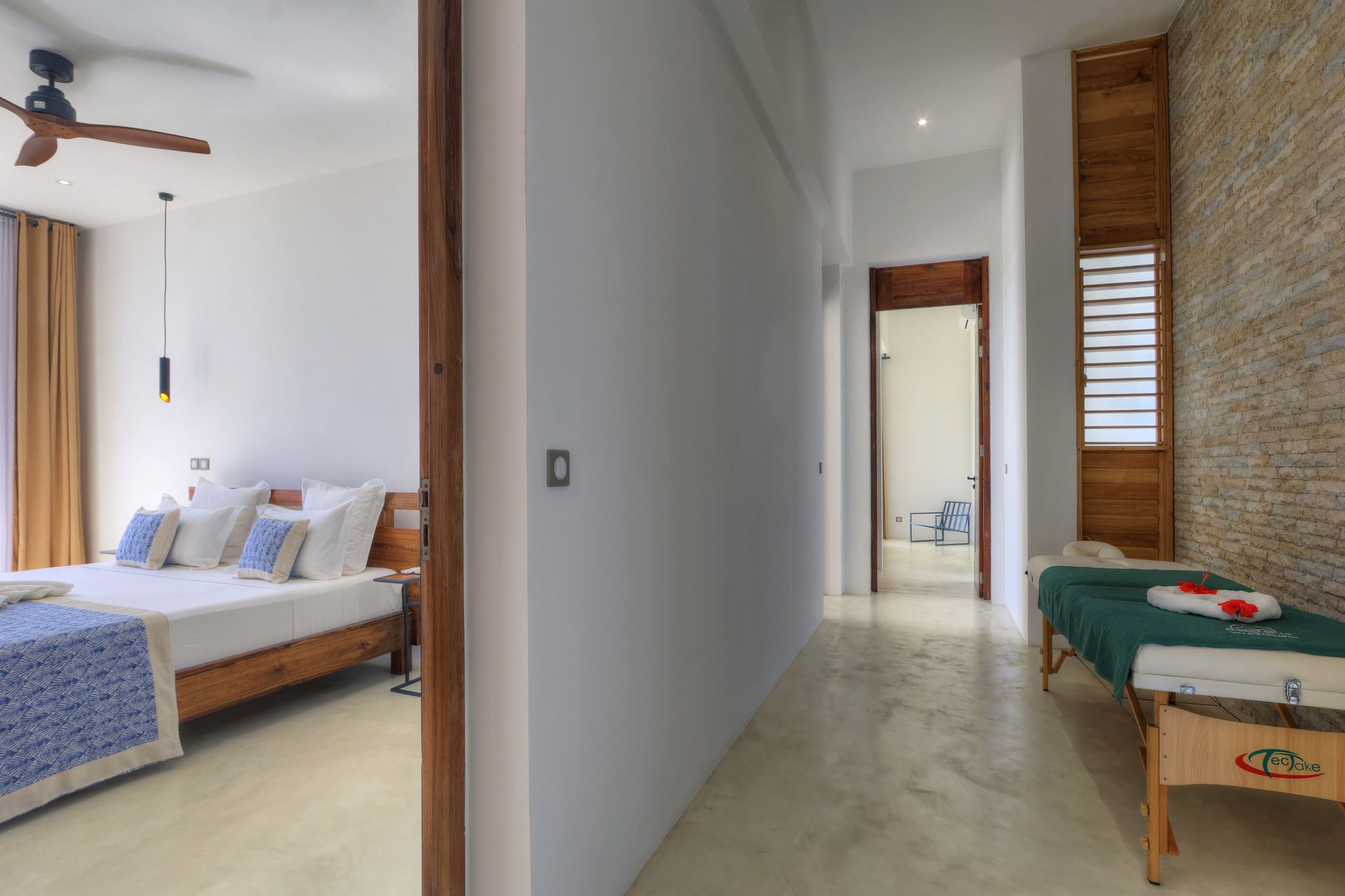 Une chambre d’hôtel avec un lit, une table de massage, un ventilateur de plafond et un mur en briques.