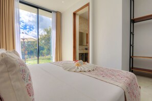 Ein Hotelzimmer mit einem großen Bett, Blick ins Freie und einem spiegeln durch einen Holzrahmen.