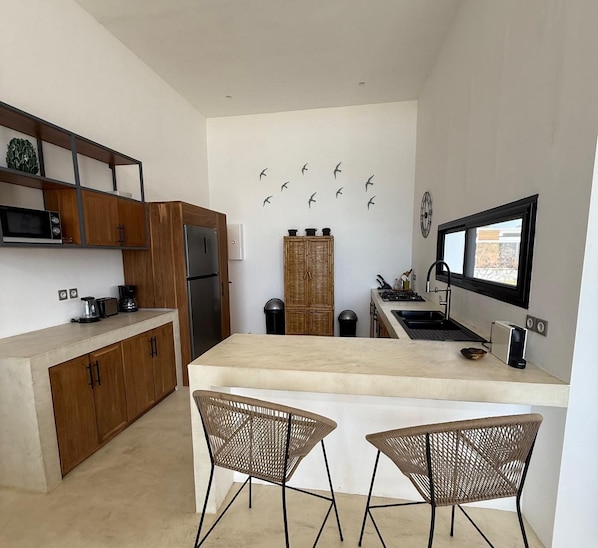 A modern kitchen with wooden cabinets, a central island, two wicker chairs, and a wall-mounted clock.