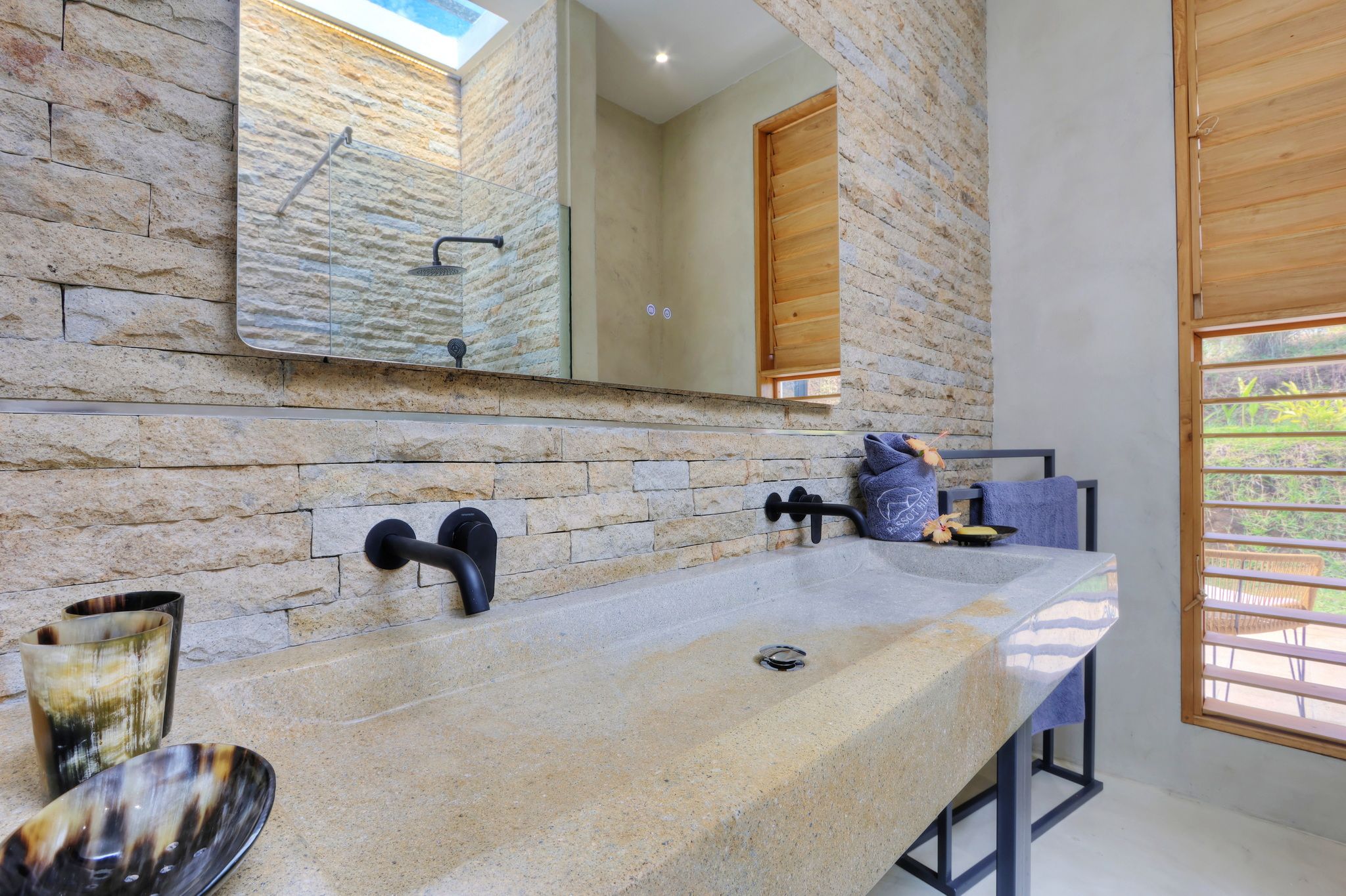 Un baño con encimera de piedra, espejo y ventana con persianas de madera.