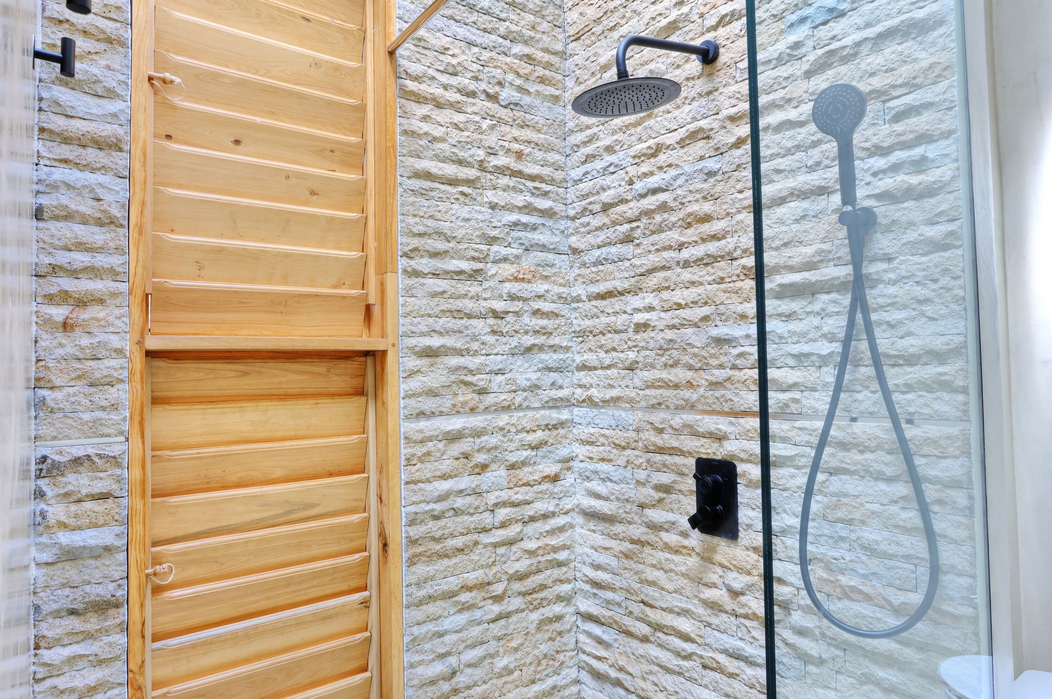 Un espace douche avec un mur à l’aspect pierre, une porte en bois et une porte en verre.