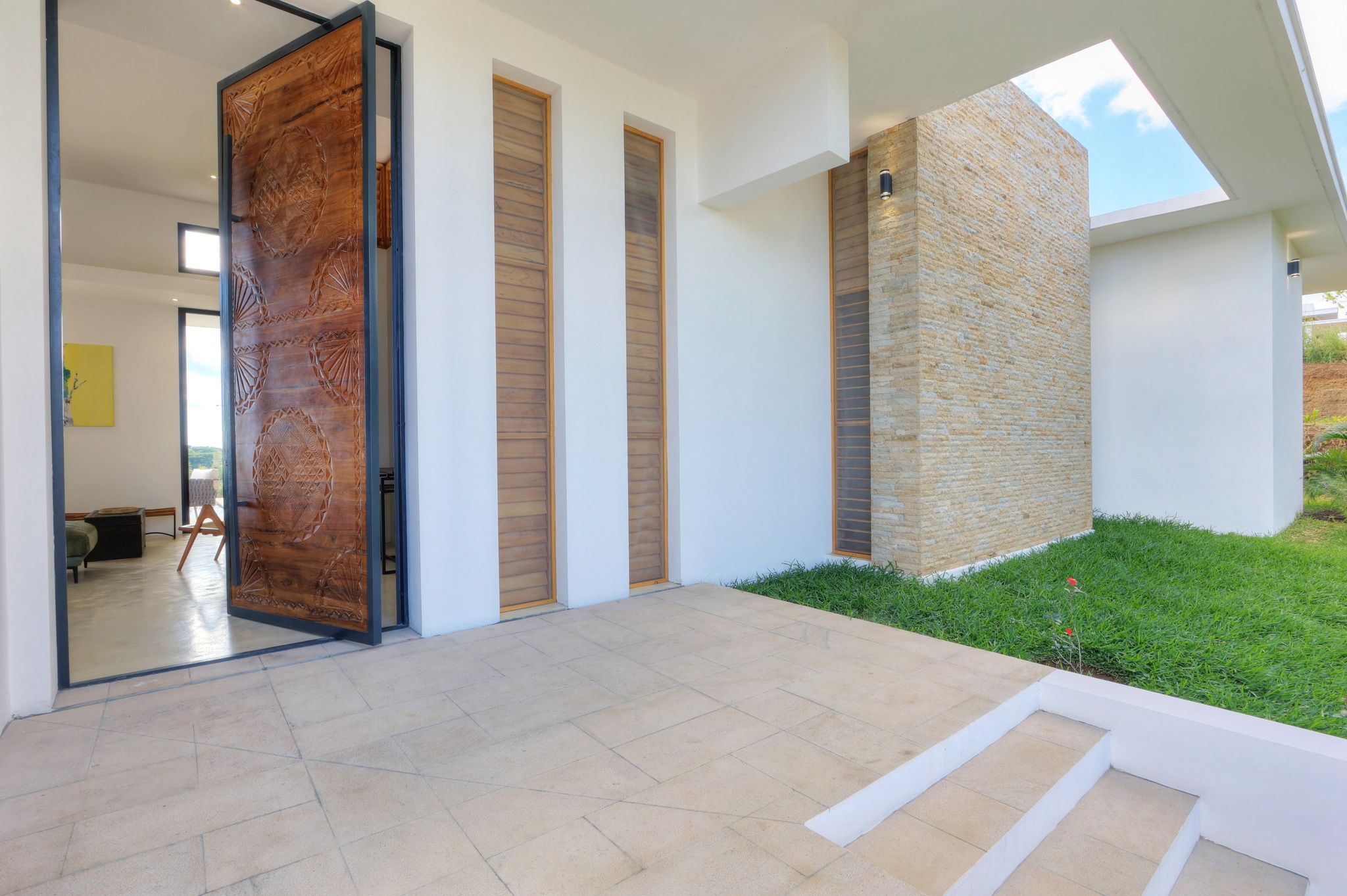 Une maison moderne avec une grande porte en bois, un mur en pierre et une pelouse bien entretenue.