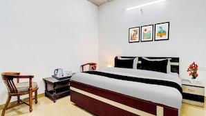 Een hotelkamer met een bed, een stoel, een nachtkastje met een lamp en een muur met drie ingelijste foto's.
