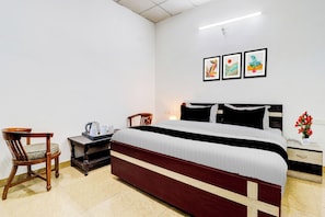 Una habitación de hotel con una cama, una silla, una mesita de noche con lámpara y una pared con tres cuadros enmarcados.