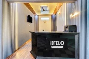 Hotellin vastaanottotiski, jossa on kello, televisio ja neonvalomainos.