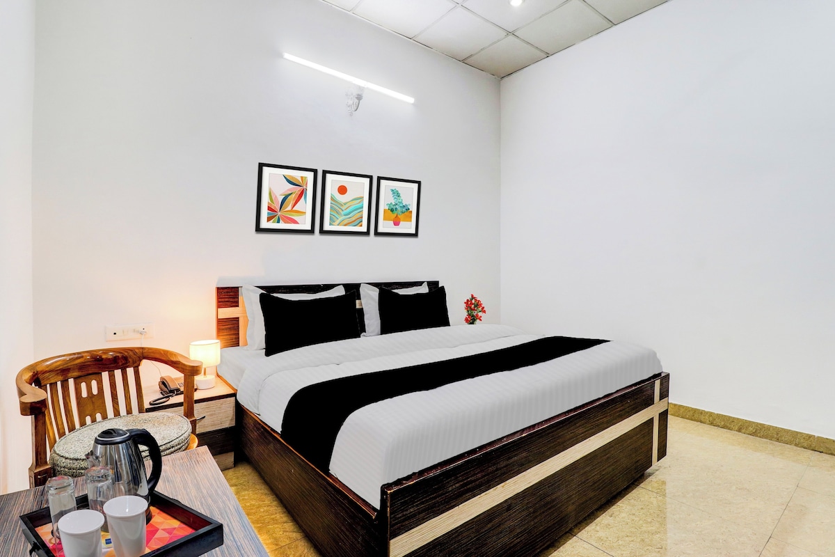 A hotel room with a bed, bedside table, lamp, and a small table with cups and a kettle.