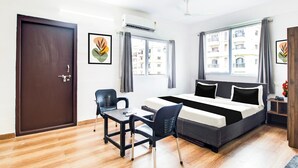 Ein Hotelzimmer mit Bett, Schreibtisch, Stuhl und einem Fenster mit Blick auf Gebäude.