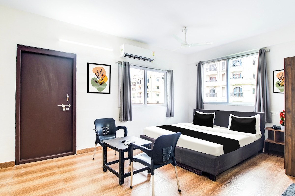 A hotel room with a bed, a desk, a chair, and a window with a view of buildings.