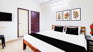 Ein Hotelzimmer mit einem Bett, einem Fernseher, einer Tür und drei gerahmten Kunstwerken an der Wand.
