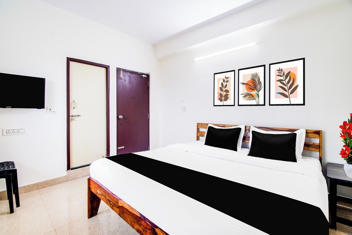 A hotel room with a bed, a TV, a door, and three framed artworks on the wall.
