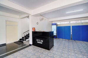 A hotel reception area with a black reception desk, a clock, a fan, and blue lockers in the background. - Hotel O Vizag IT Hill Rushikonda (Visakhapatnam)