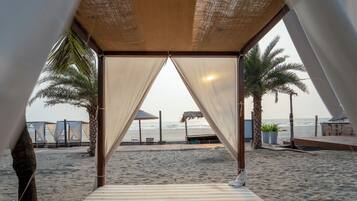 A beach view from a tent with a striped floor, palm trees, and beach umbrellas.