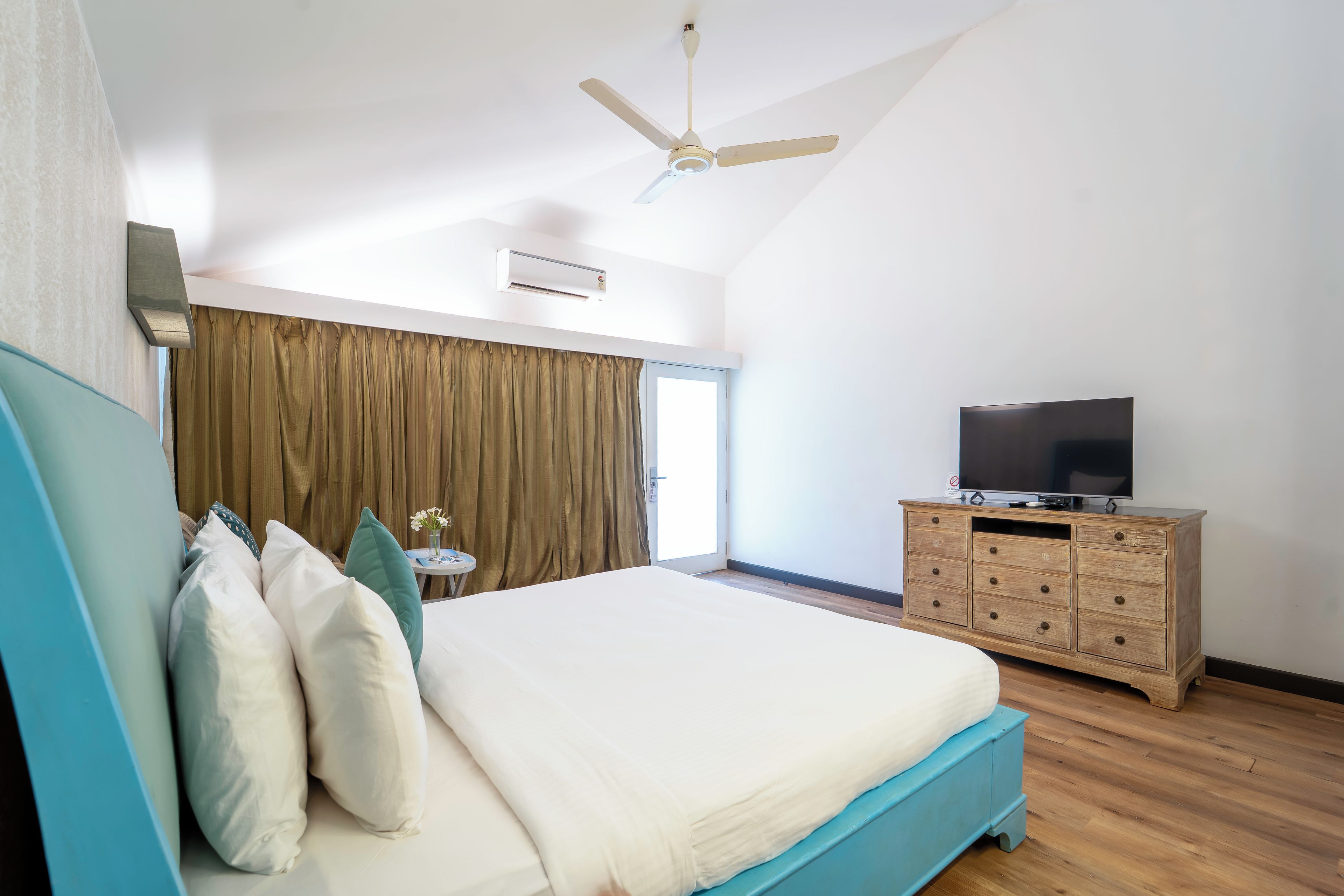 A bedroom with a bed, a television on a wooden dresser, and a ceiling fan.