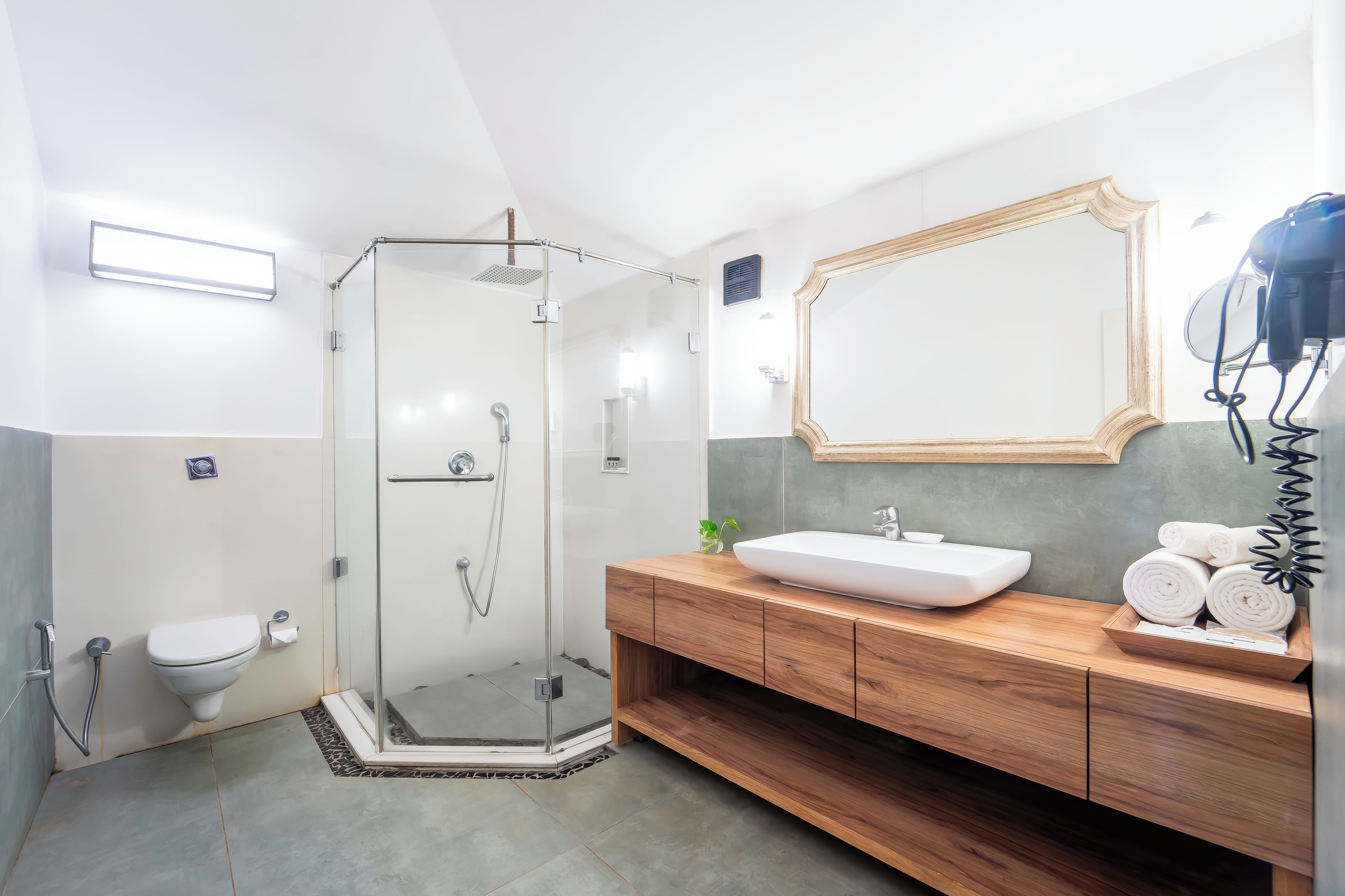 Un baño moderno con ducha envuelta en vidrio, tocador de madera y un espejo grande.