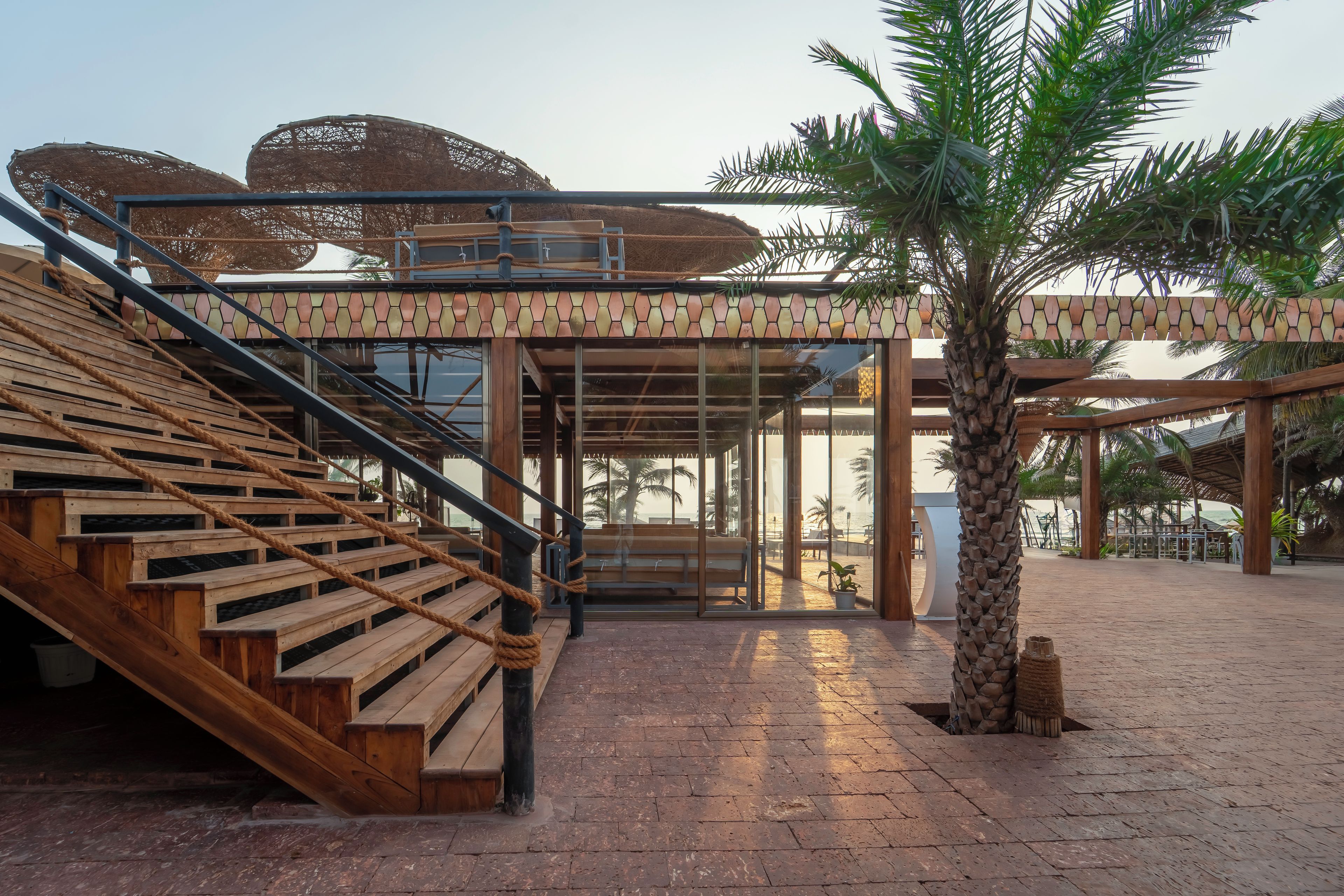 Una escalera de madera lleva a un área cubierta con una palmera y vista a la playa.