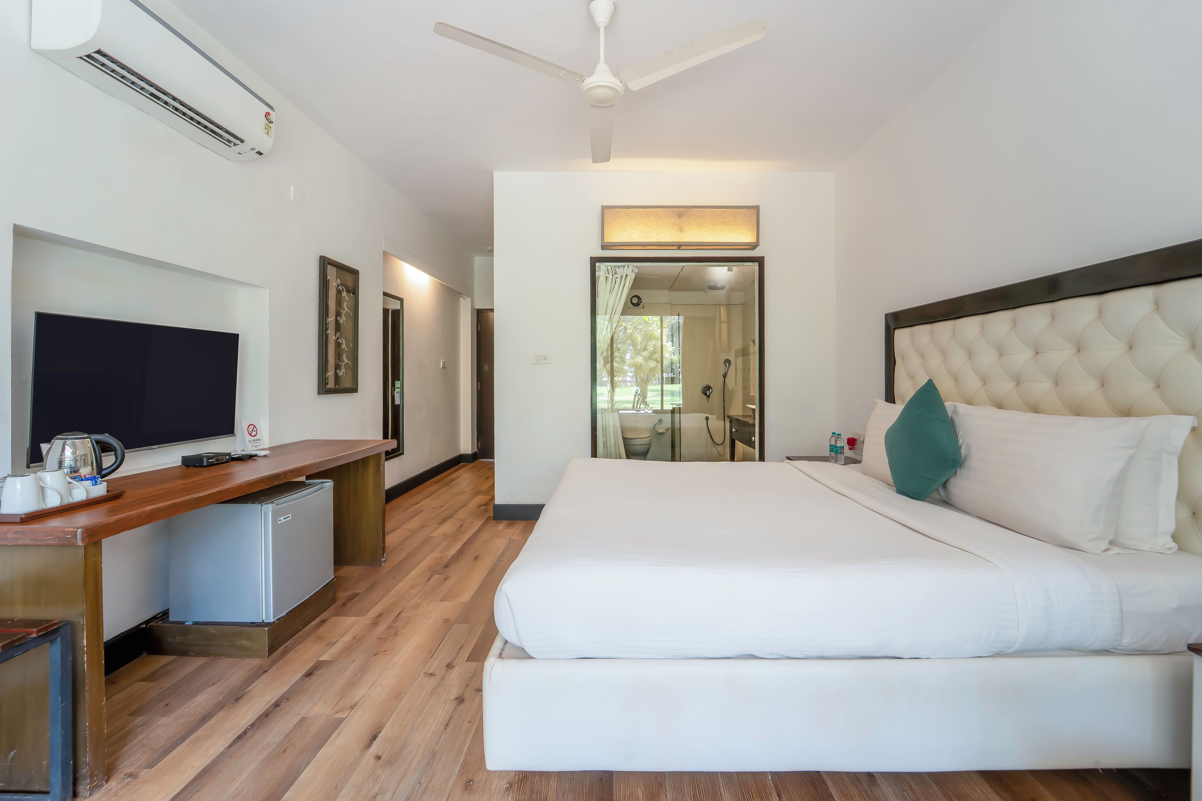 Una habitación de hotel con una cama, un escritorio con televisor y un ventilador de techo.