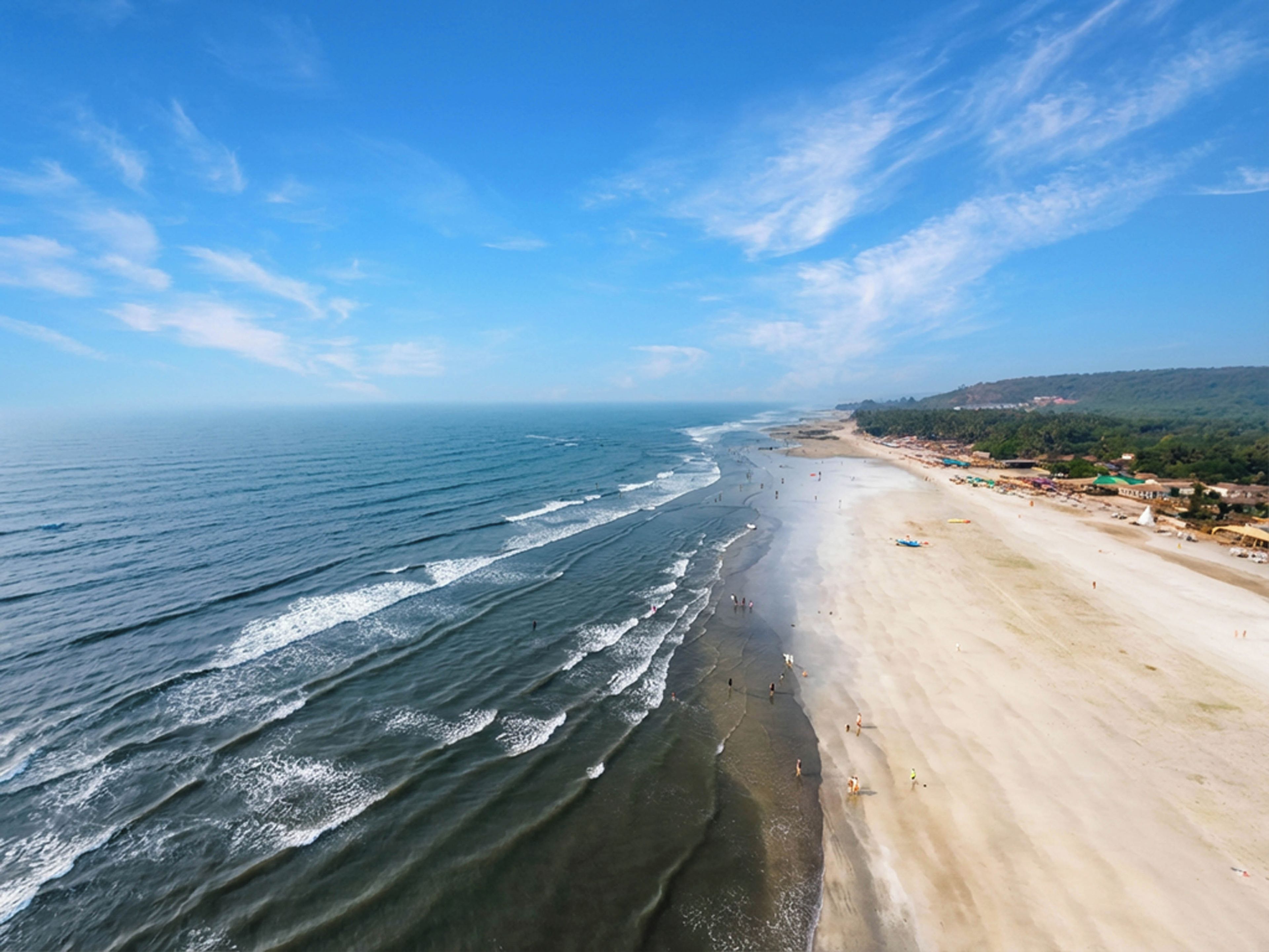 A coastal beach with waves, a sandy shore, and distant buildings.