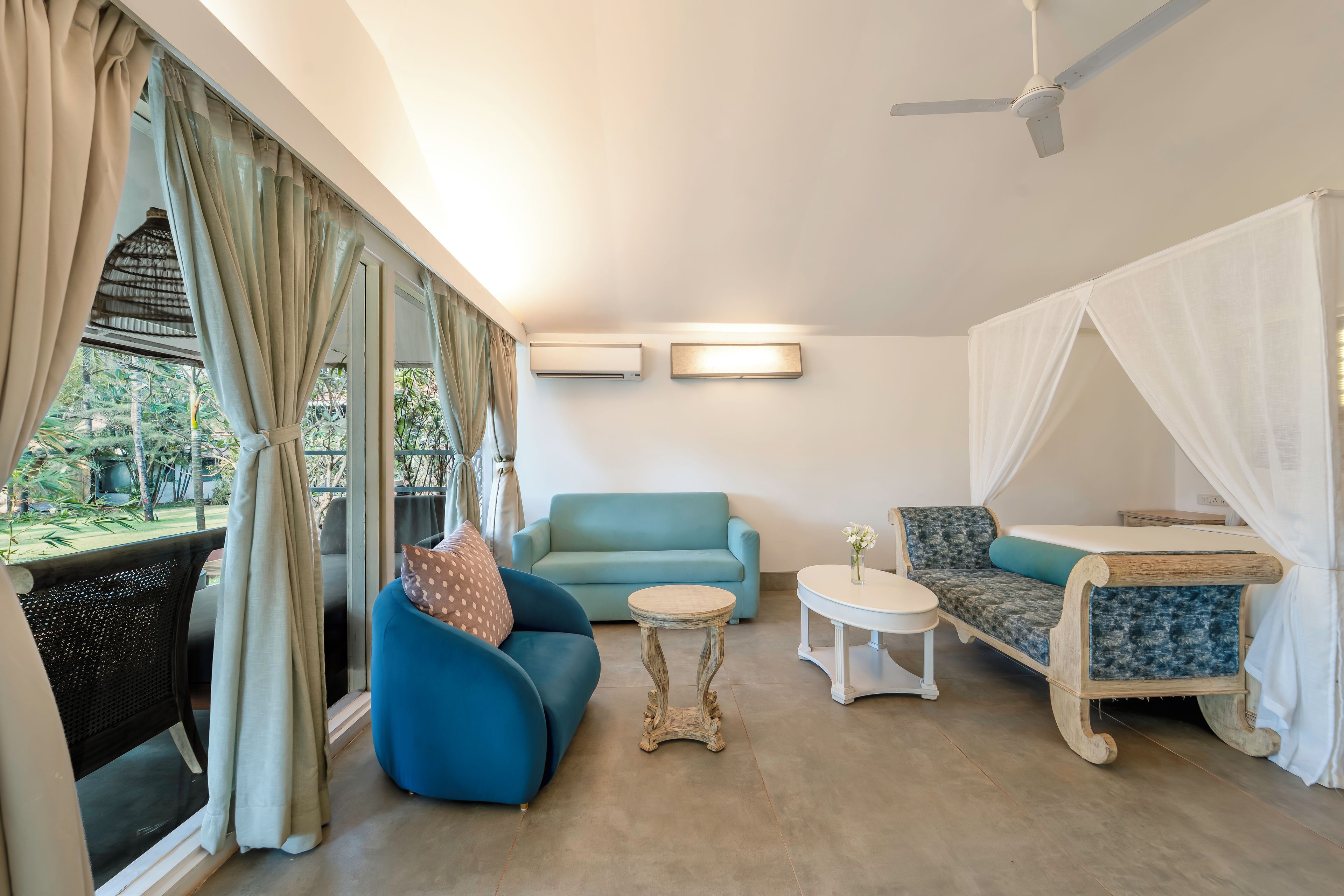 Una habitación con un sofá azul, una mesita redonda pequeña, una cama con dosel y un ventilador de techo.