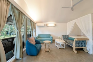 A room with a blue sofa, a small round table, a canopy bed, and a ceiling fan. - Marbela Beach Resort  (Morjim)