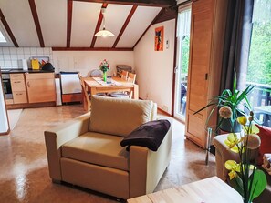 Een gezellige woonkamer met een bank, een eettafel met stoelen, een keuken met kasten en apparatuur, en een balkon met planten.