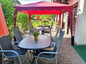 Une terrasse extérieure avec une table et des chaises, un parasol rouge et une vue sur le jardin.