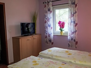 Een slaapkamer met een bed, een televisie op een houten kast en een raam met gordijnen.