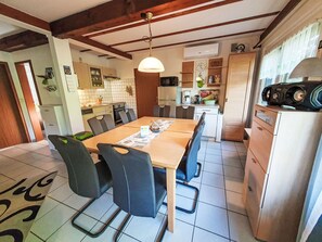 A dining area with a wooden table and chairs, a kitchen in the background, and a ceiling with exposed beams. - Ferienhaus Bussard by Interhome (Frielendorf)
