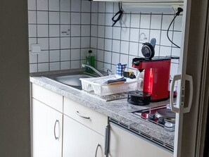 Een keuken met witte kastjes, een granieten aanrecht, een rode koffiezetapparaat en een spoelbak.