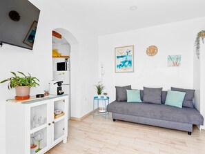 Ein modernes Wohnzimmer mit einem grauen Sofa, einer weißen Kommode und einem kleinen runden Tisch mit einer Pflanze.