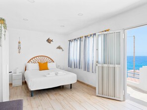 Ein Schlafzimmer mit einem Bett, einem Nachttisch, einem Fenster mit Vorhängen und Meerblick.
