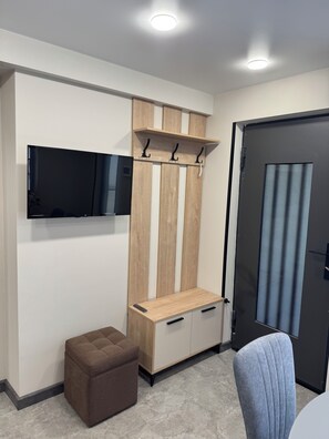 A modern room with a flat-screen TV mounted on the wall, a wooden panel wall with a bench, a small ottoman, and a grey upholstered chair. - Modern 1-bedroom apartment in cool Yerevan with AC (Yerevan)