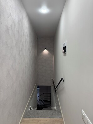 Um corredor estreito com paredes estampadas, uma escada e uma luminária no teto.
