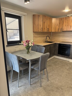 A modern kitchen with wooden cabinets, a built-in oven, and a dining area with grey chairs and a vase of flowers. - Modern 1-bedroom apartment in cool Yerevan with AC (Yerevan)