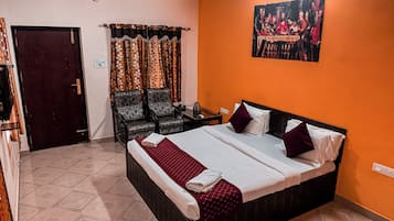 A hotel room with a large bed, two chairs, a desk, and a painting on the wall.