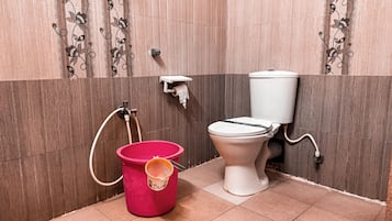 A bathroom with a toilet, a pink bucket, and a toilet paper holder on the wall.