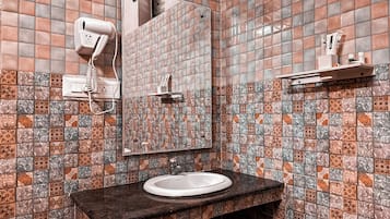 A bathroom with a tiled wall, a sink, a mirror, and a towel dispenser.