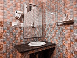 A bathroom with a tiled wall, a sink, a mirror, and a towel dispenser.