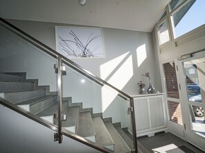 Una escala moderna amb baranes de vidre, una obra d'art abstracta penjada a la paret i una porta que dona a l'exterior.