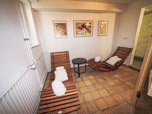 Ein Spa-Raum mit Holzliegen, einem kleinen runden Tisch und drei gerahmten Bildern an der Wand.