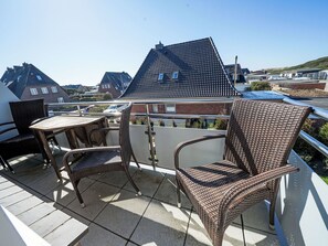 Varanda com mobiliário de vime, piso de azulejos e vista para casas e um estacionamento.