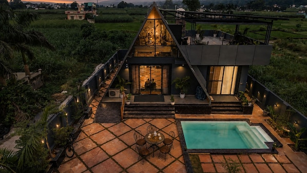 A modern villa with a swimming pool, outdoor seating, and a view of the surrounding landscape.