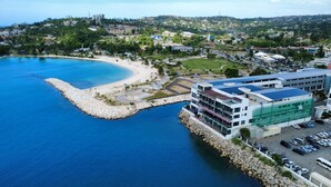 Una zona costanera amb una platja, un moll de pedra i un edifici modern amb un aparcament.