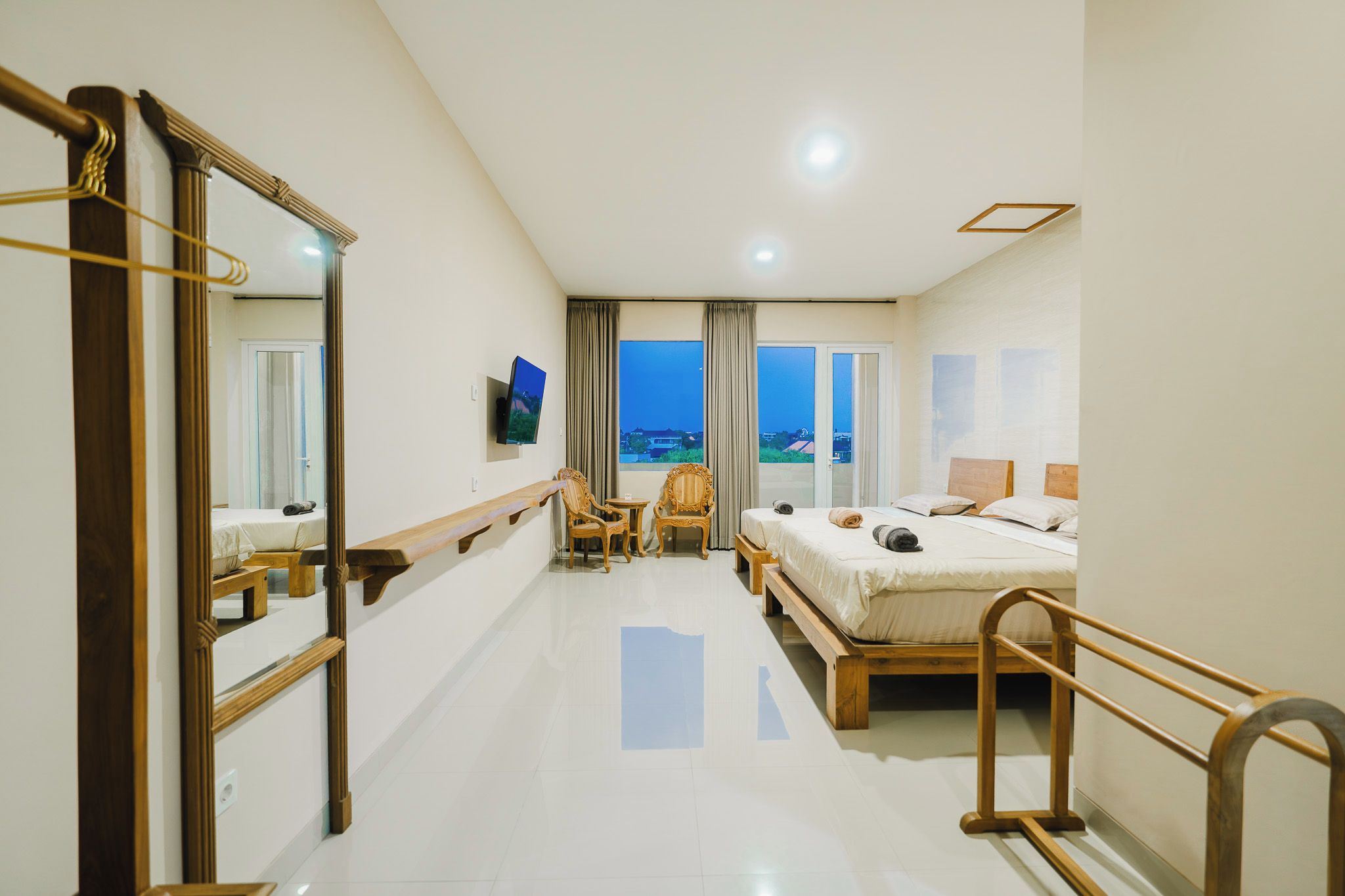 Una habitación de hotel con cama, televisor, sillón, escritorio y un espejo grande.