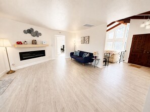 Un salón espacioso con chimenea, un sofá azul y una zona de comedor con una mesa y sillas de madera.