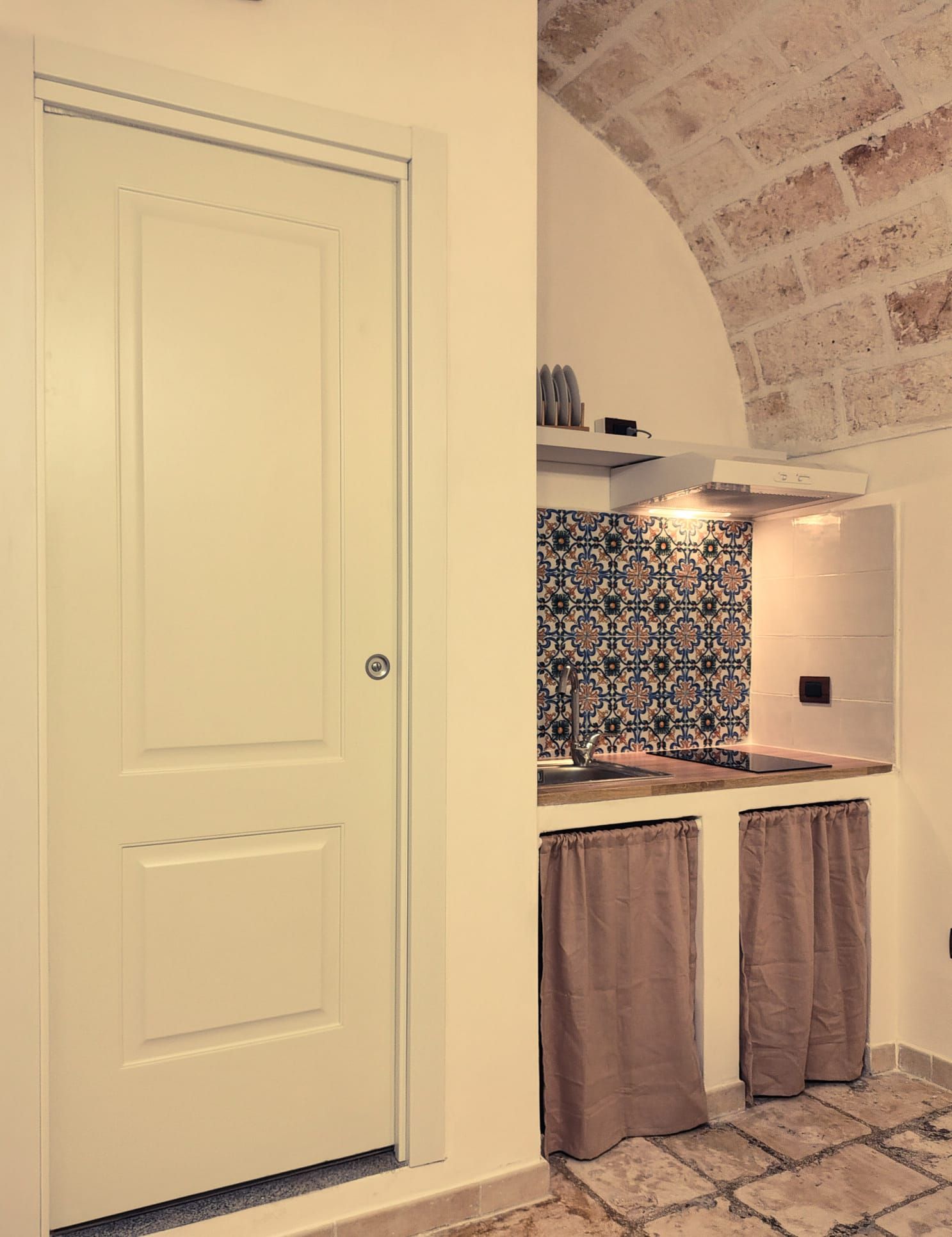 Una cucina con una porta bianca, zoccolo paraschizzi decorato e parete in mattoni.