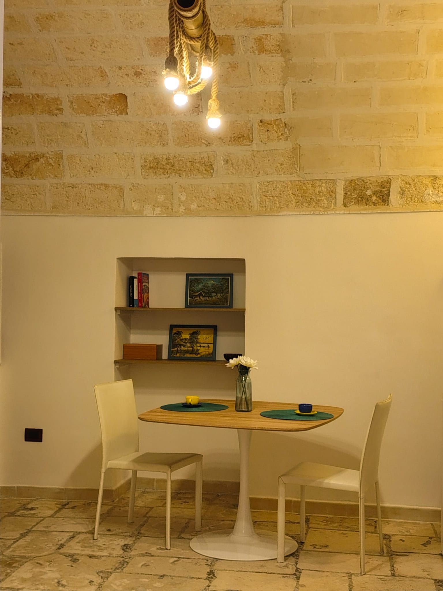 Una stanza con un muro in mattoni, un tavolo rotondo con sedie, una libreria e un lampadario.