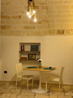 A room with a brick wall, a round table with chairs, a bookshelf, and a hanging light fixture. - Dimora Pietre Gemelle, Modugno, Bari (Modugno)