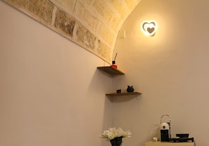 A bathroom with a white wall, a heart-shaped light fixture, a shelf with a black cat figurine, a vase with white flowers, and a coffee machine. - Dimora Pietre Gemelle, Modugno, Bari (Modugno)