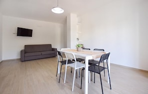 A modern living space with a sofa, dining table, chairs, and a TV mounted on the wall. - Awesome apartment in Agropoli with house a panoramic view (Agropoli)